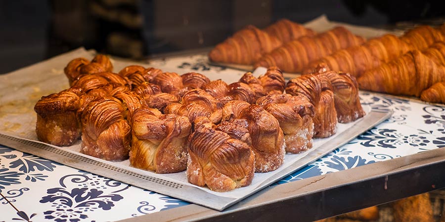 Freshly baked browned pastries sit on a metal tray in a cafe window. 